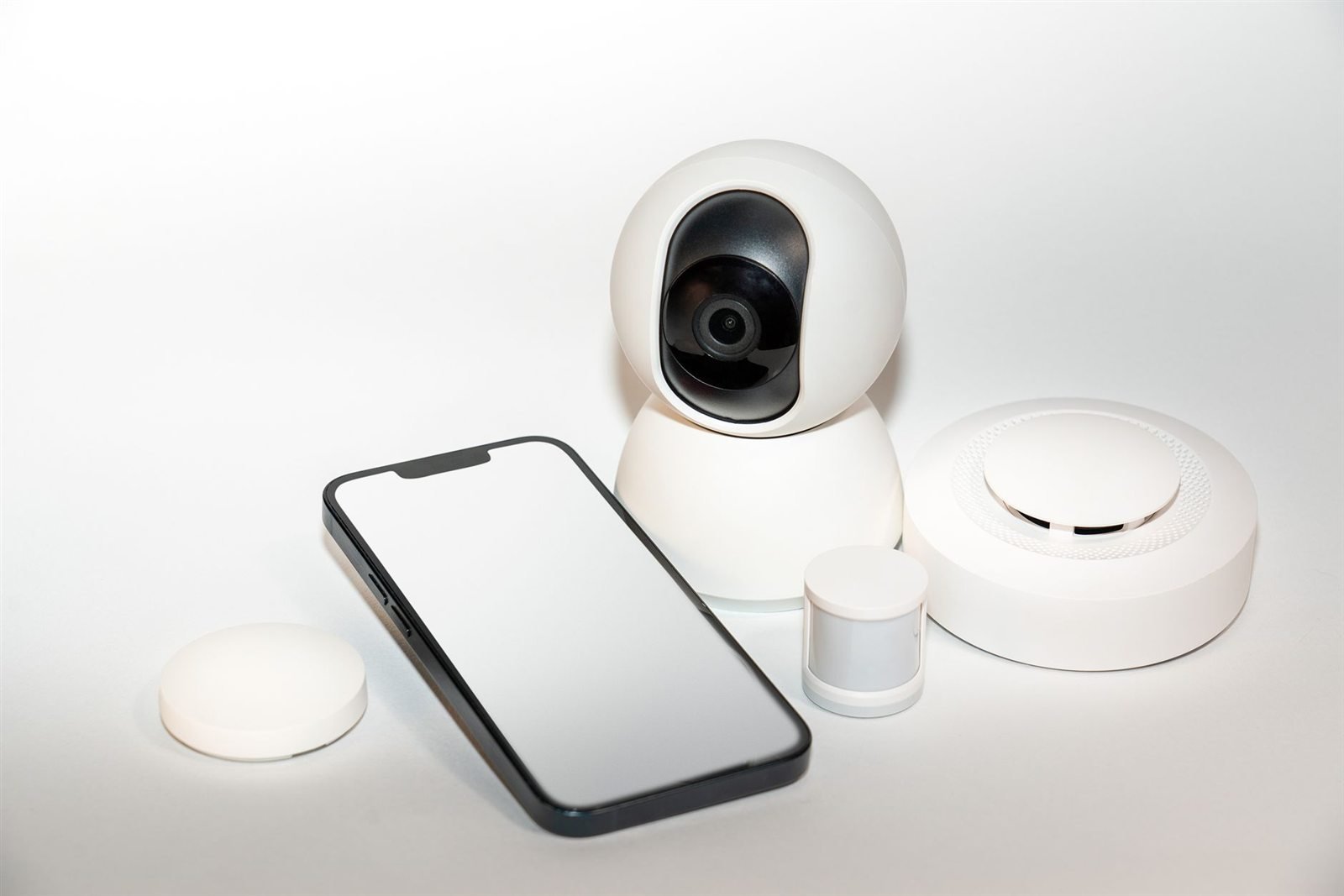 A smartphone beside small round white smart home sensors and a camera