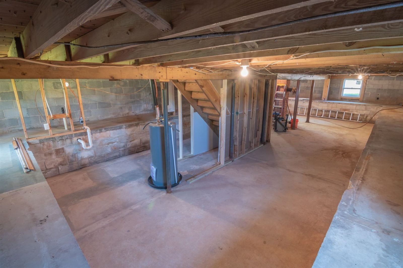 An unfinished basement with support columns, exposed joists and utility equipment