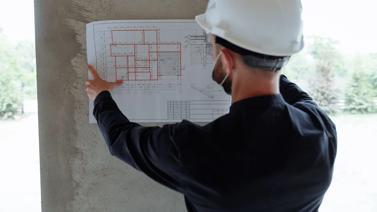 A person in a hard hat holding drawings up against a concrete structure