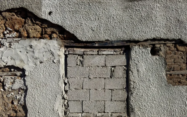 A weathered wall with render broken away, exposing the masonry beneath
