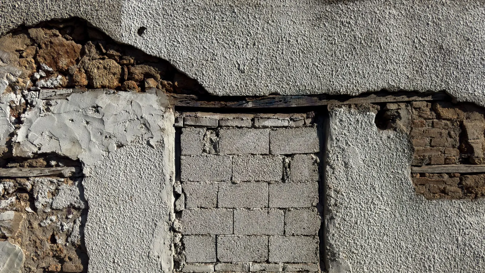 A weathered wall with render broken away, exposing the masonry beneath