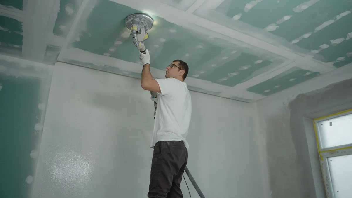 A worker finishing a ceiling overhead with a hand tool