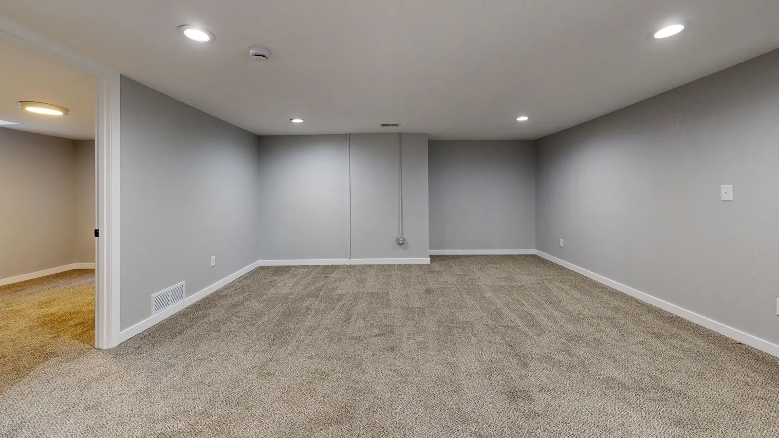 A clean, empty finished basement room with carpet and painted walls