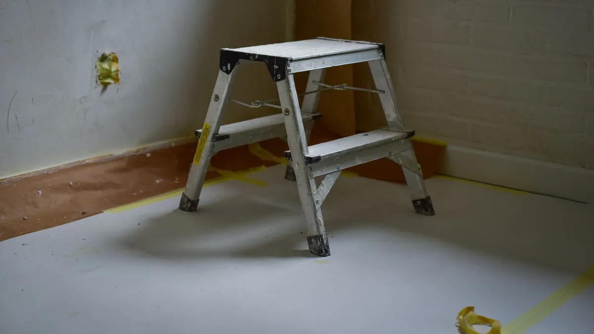 A metal ladder standing on a taped-off bare floor in an empty room