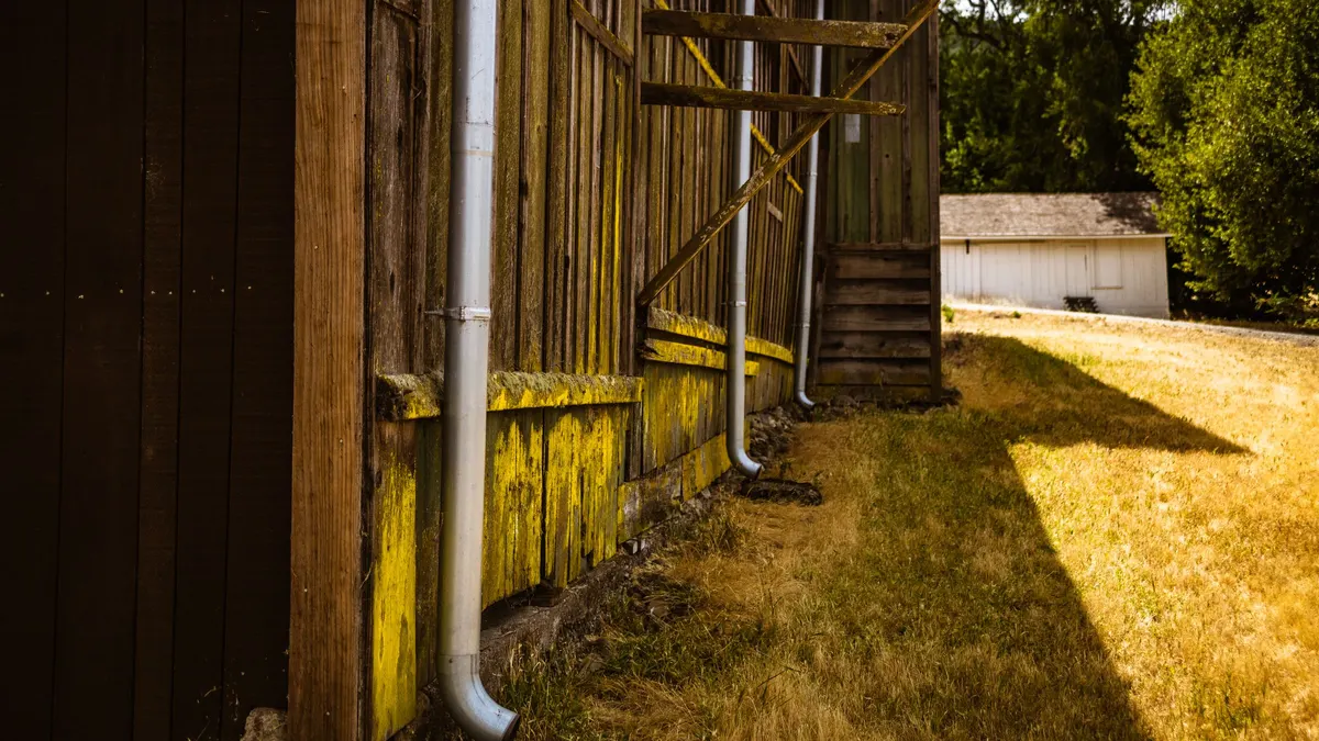 A downspout running down a timber building wall and discharging onto the ground beside it