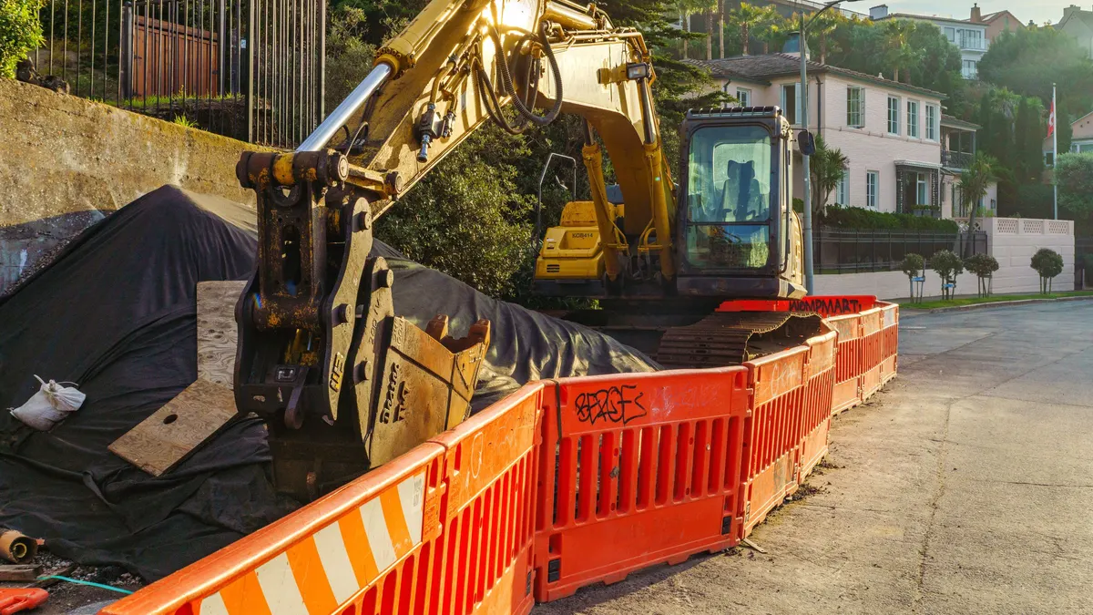 An excavator digging an open trench alongside a house foundation