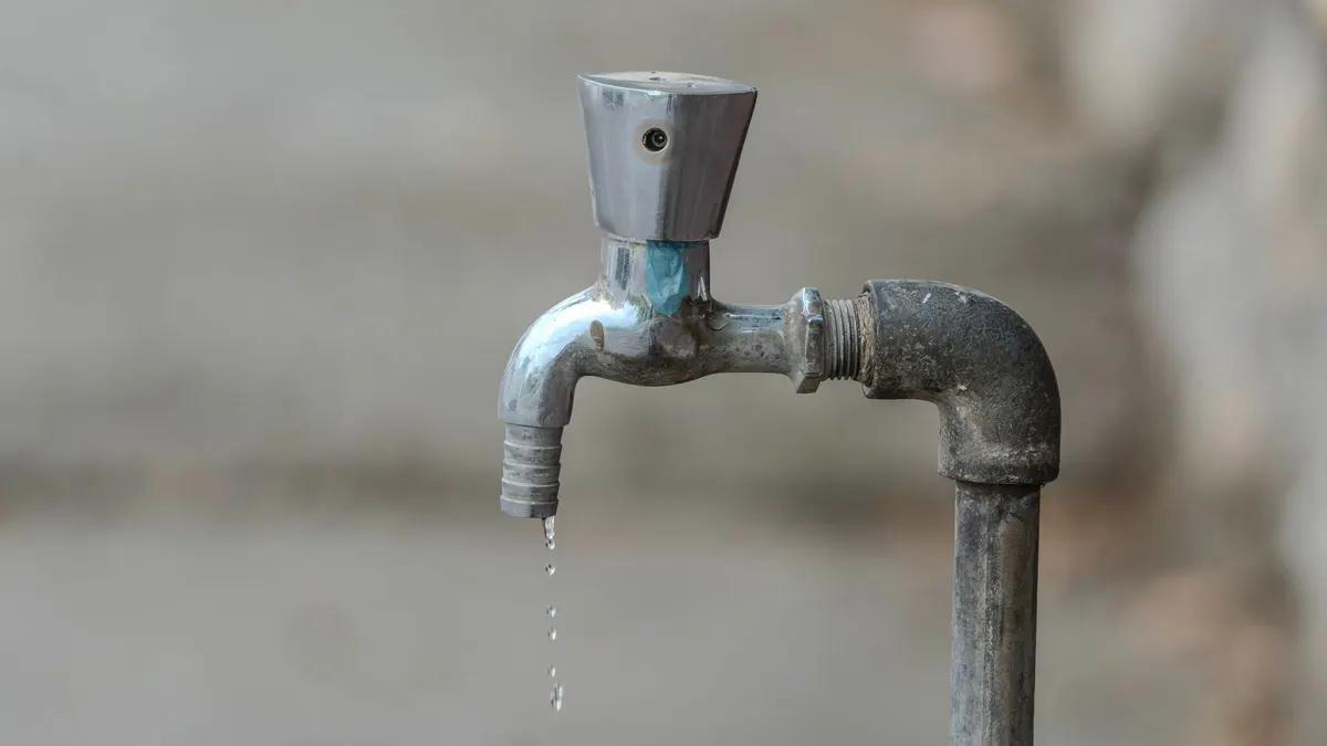 An outdoor water tap with a droplet forming at its spout