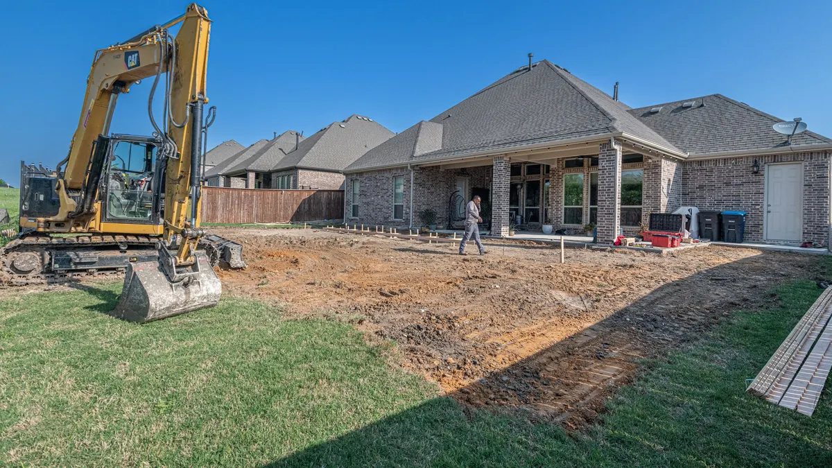 An excavator and disturbed ground at a construction site beside a house