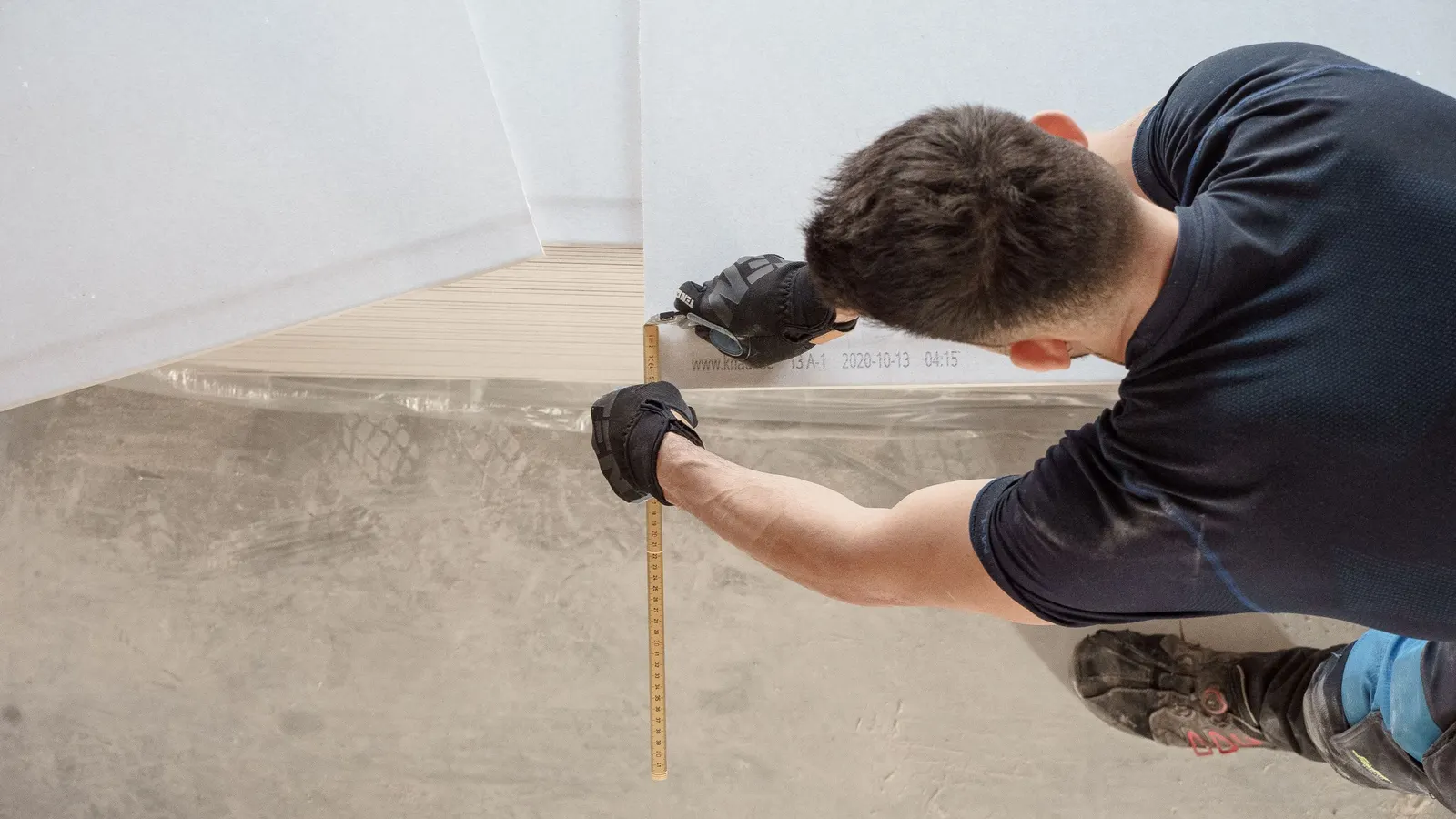 A worker kneeling to measure along the base of an interior wall