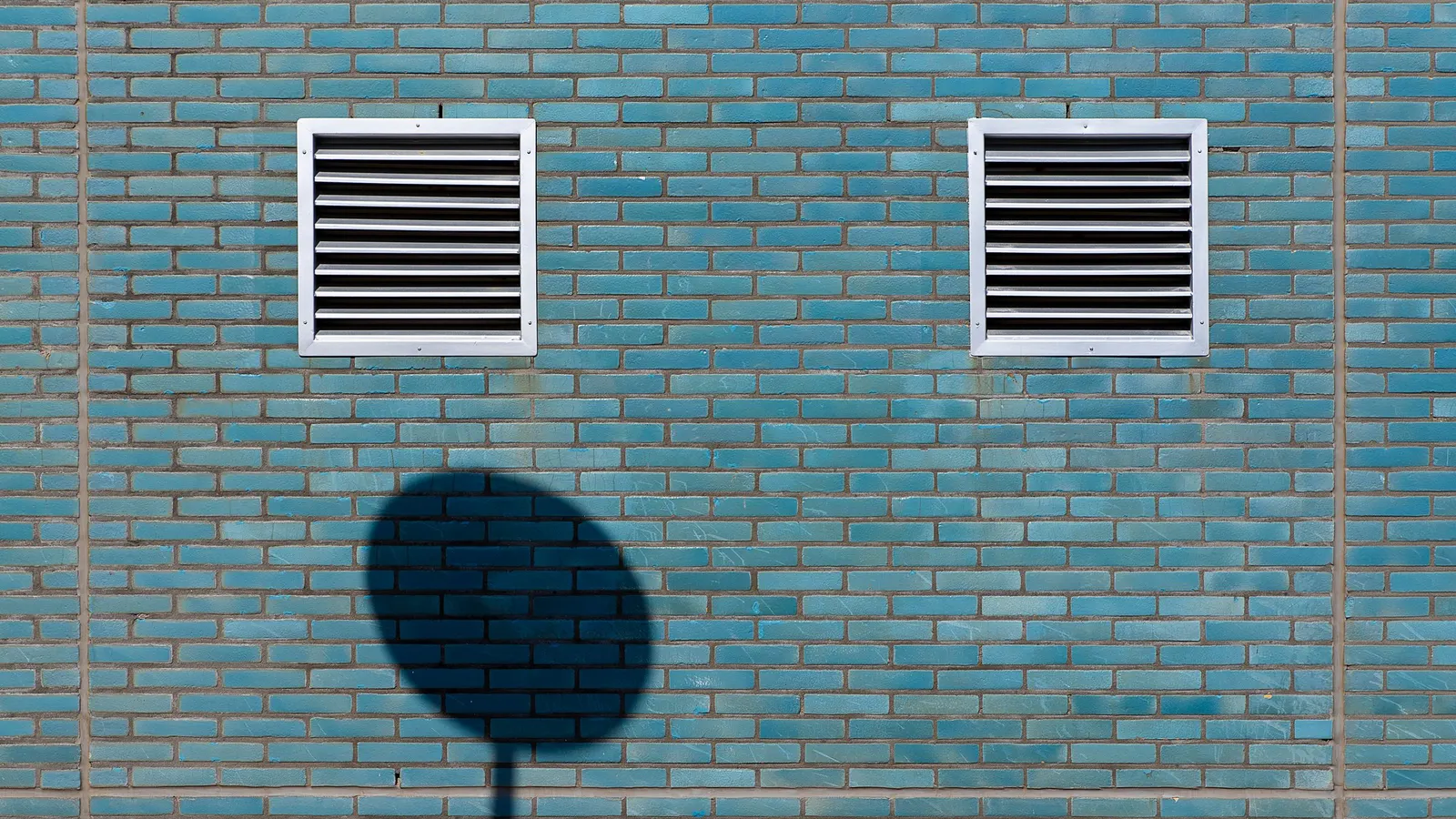 Two louvred vents set into a painted brick wall