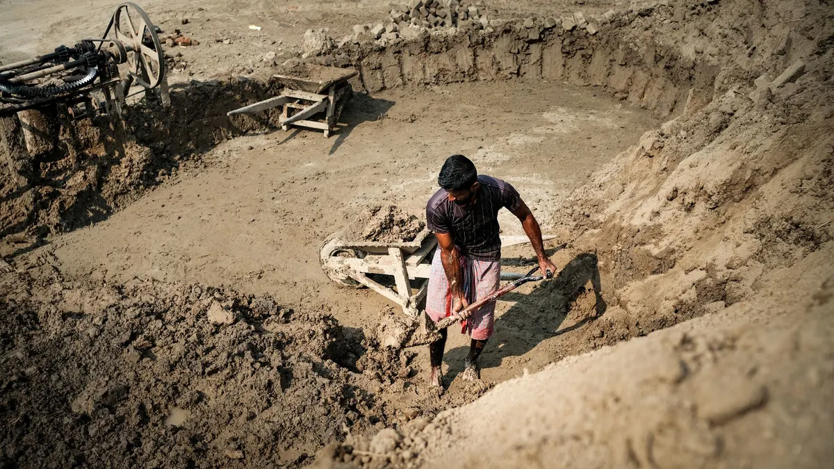 A person digging by hand in a trench of sandy soil