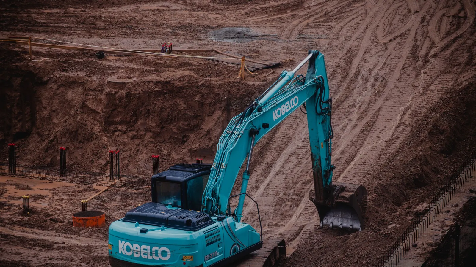 An excavator digging into deep reddish earth at a site