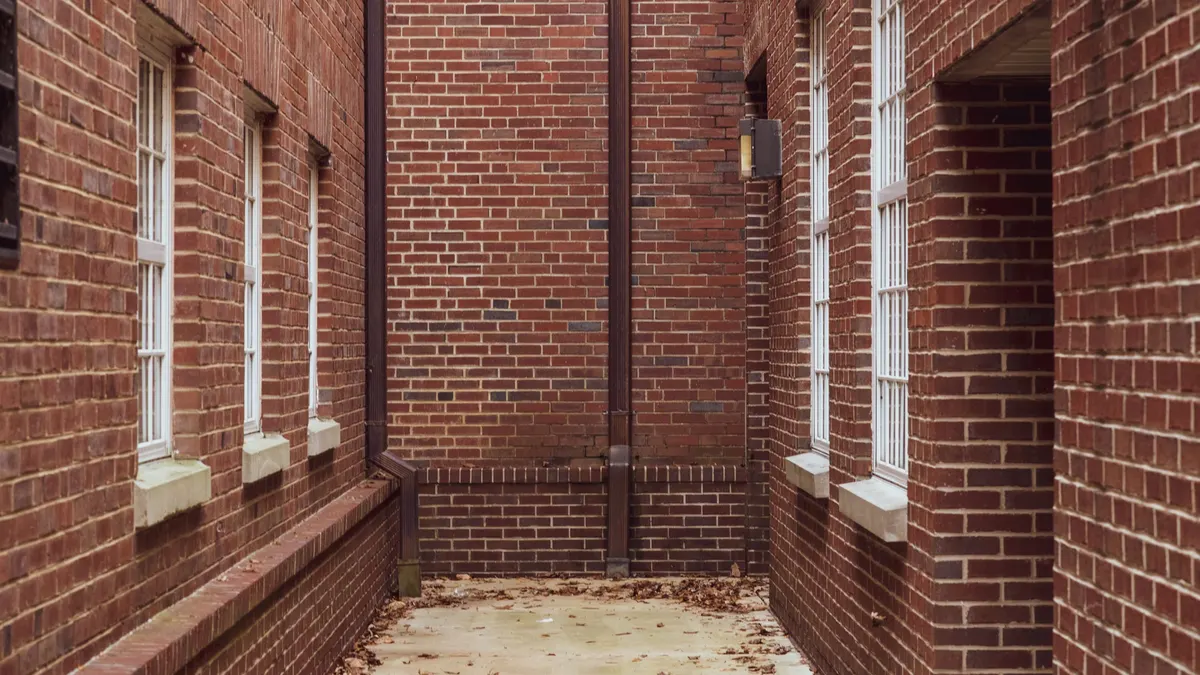 A narrow red brick alleyway with fallen autumn leaves
