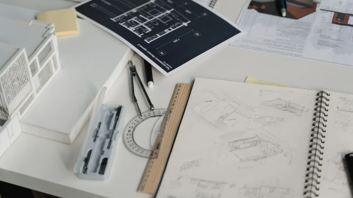 A desk with drawings, a scale rule and a notebook laid out