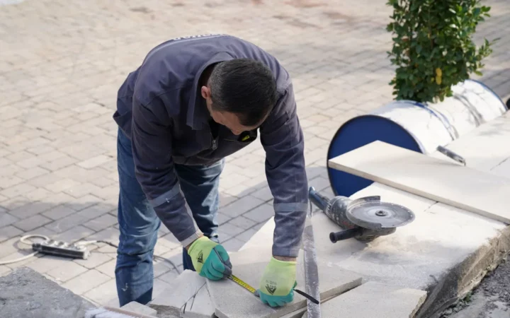 A construction worker measuring and setting paving at ground level