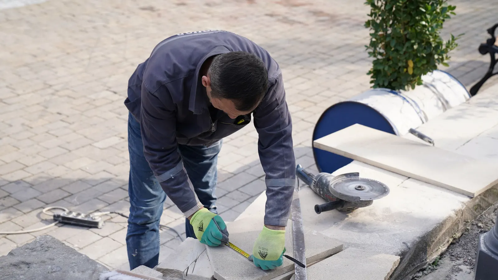 A construction worker measuring and setting paving at ground level