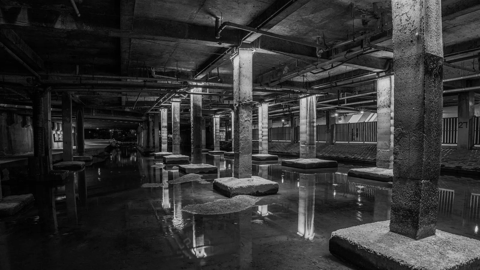 Standing water across the floor of a dark underground space with concrete columns