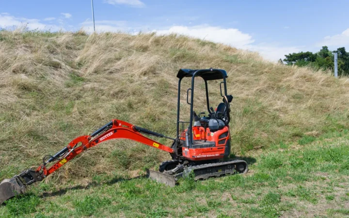 A compact excavator standing on grass in front of a hillside