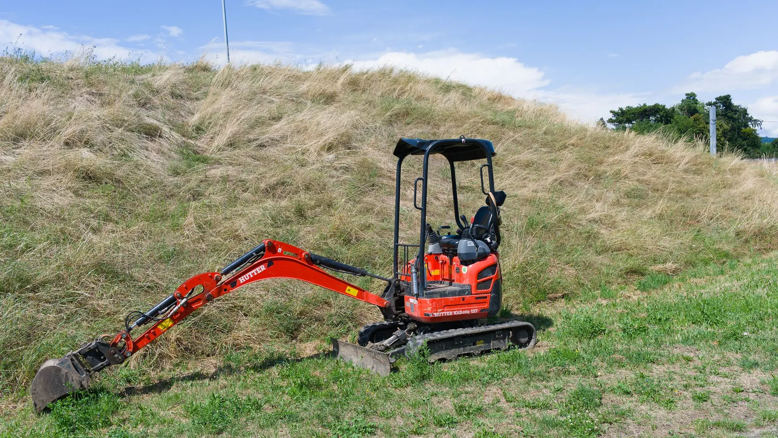 A compact excavator standing on grass in front of a hillside