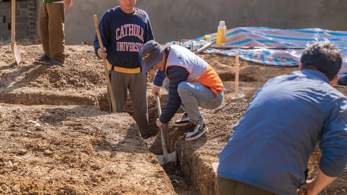 Workers digging a narrow trench by hand in bare soil