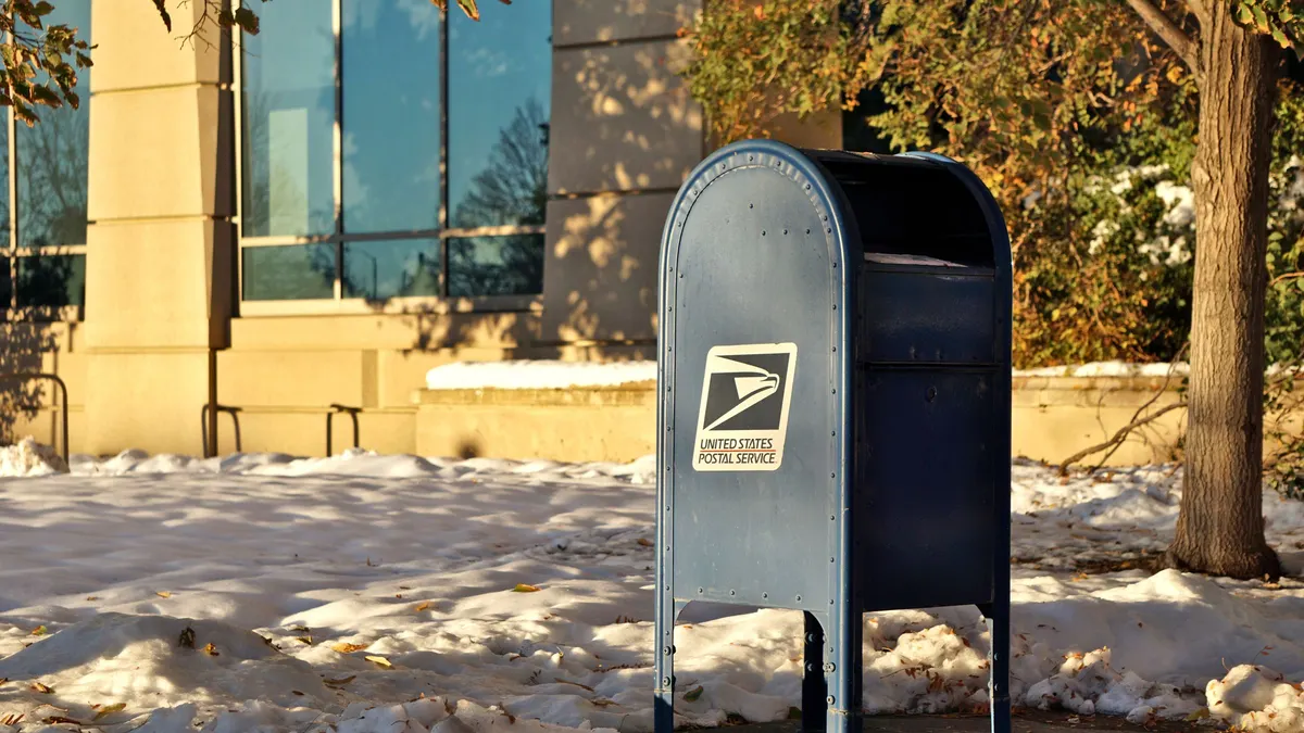 A blue United States Postal Service collection box on a street in winter