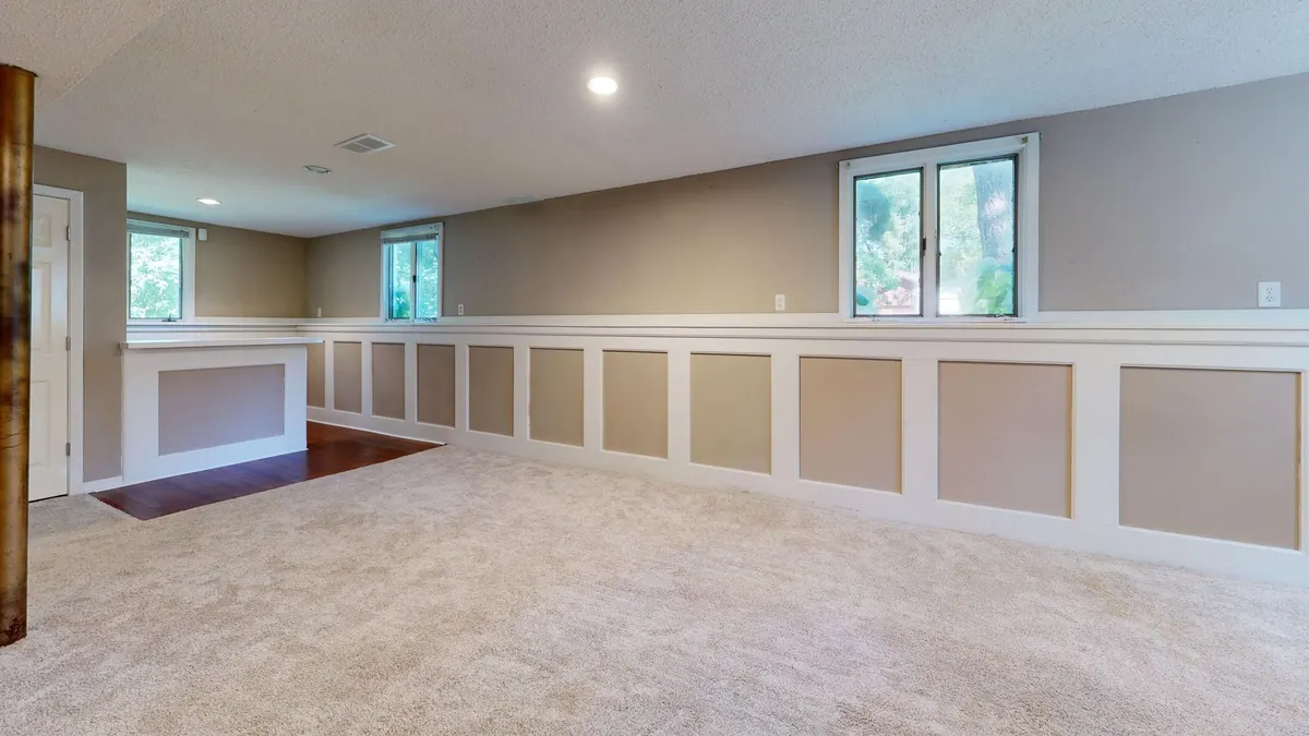 A finished basement room with carpet and small windows near the ceiling