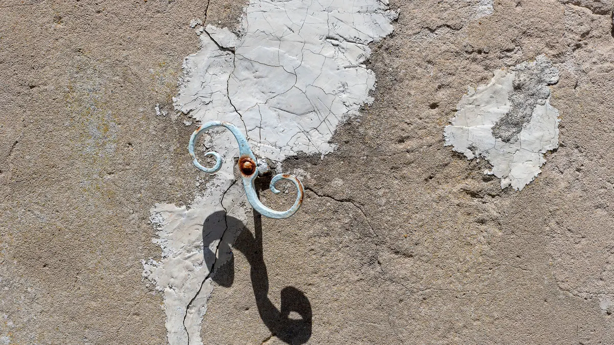 A rusted metal hook fixed into a cracked, textured masonry wall