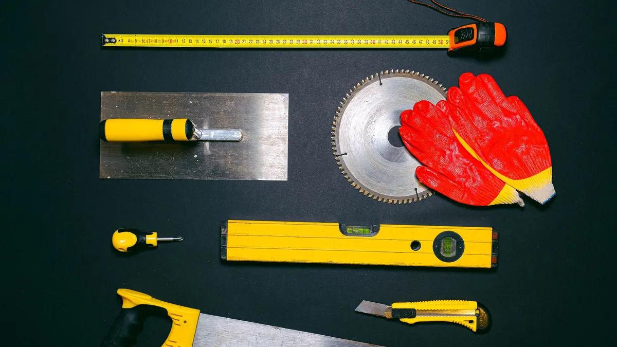 A trowel, spirit level, saw blade and gloves laid out on a dark surface
