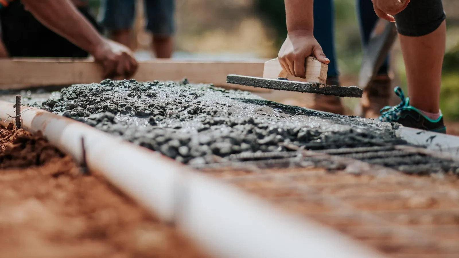 Hands using a trowel to work wet cement mix into a form at ground level
