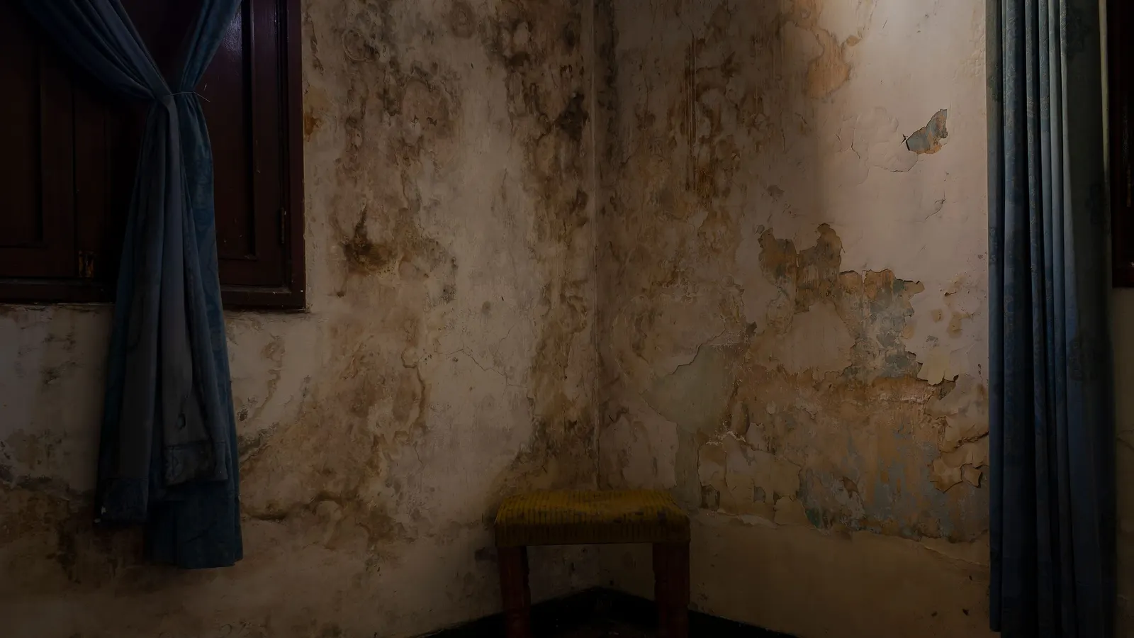 An abandoned room with peeling, water-stained walls and a small stool