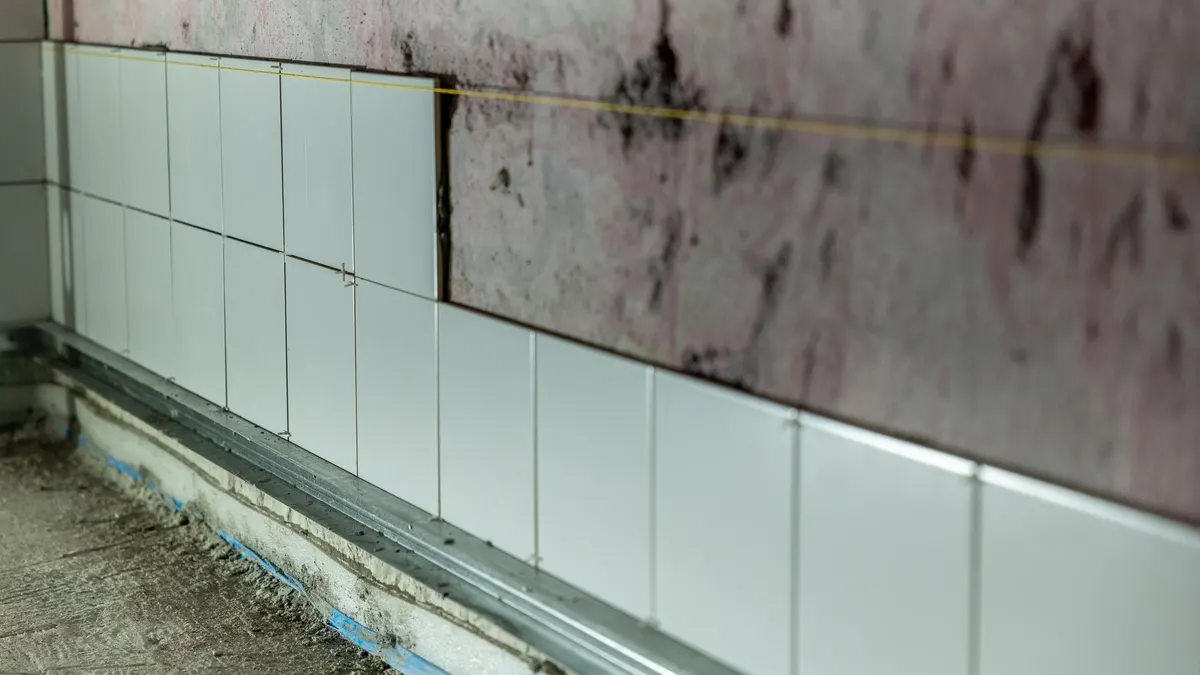 A partially tiled wall in a construction area showing dark staining above the tiles