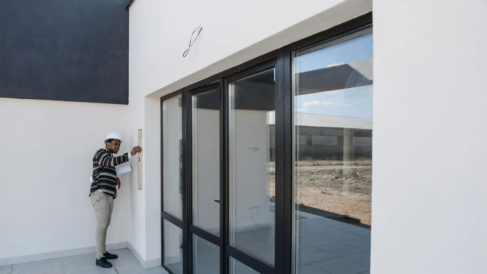An architect in a hard hat inspecting a glass door in a modern house