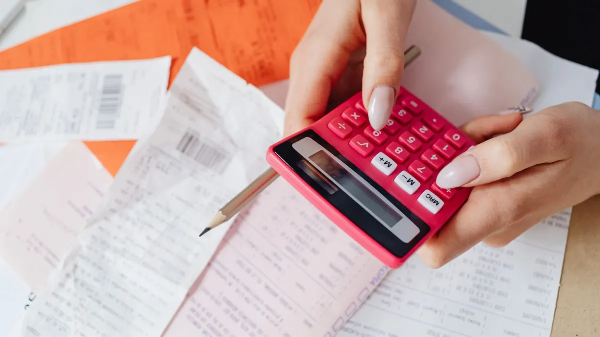 A hand using a calculator beside a stack of printed bills and paperwork