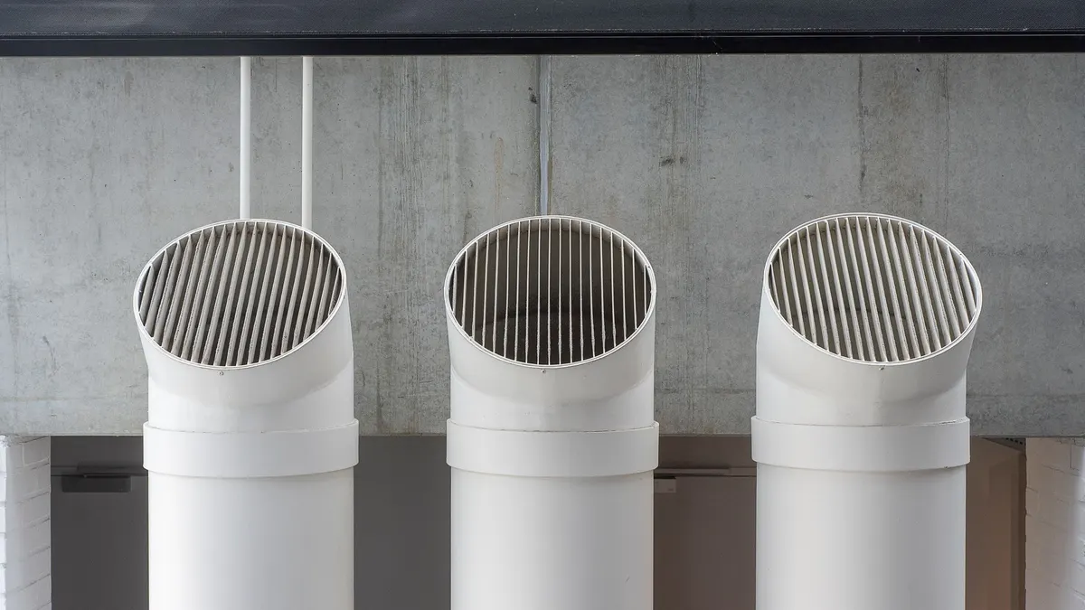 Three white pipe terminations standing side by side against a concrete wall