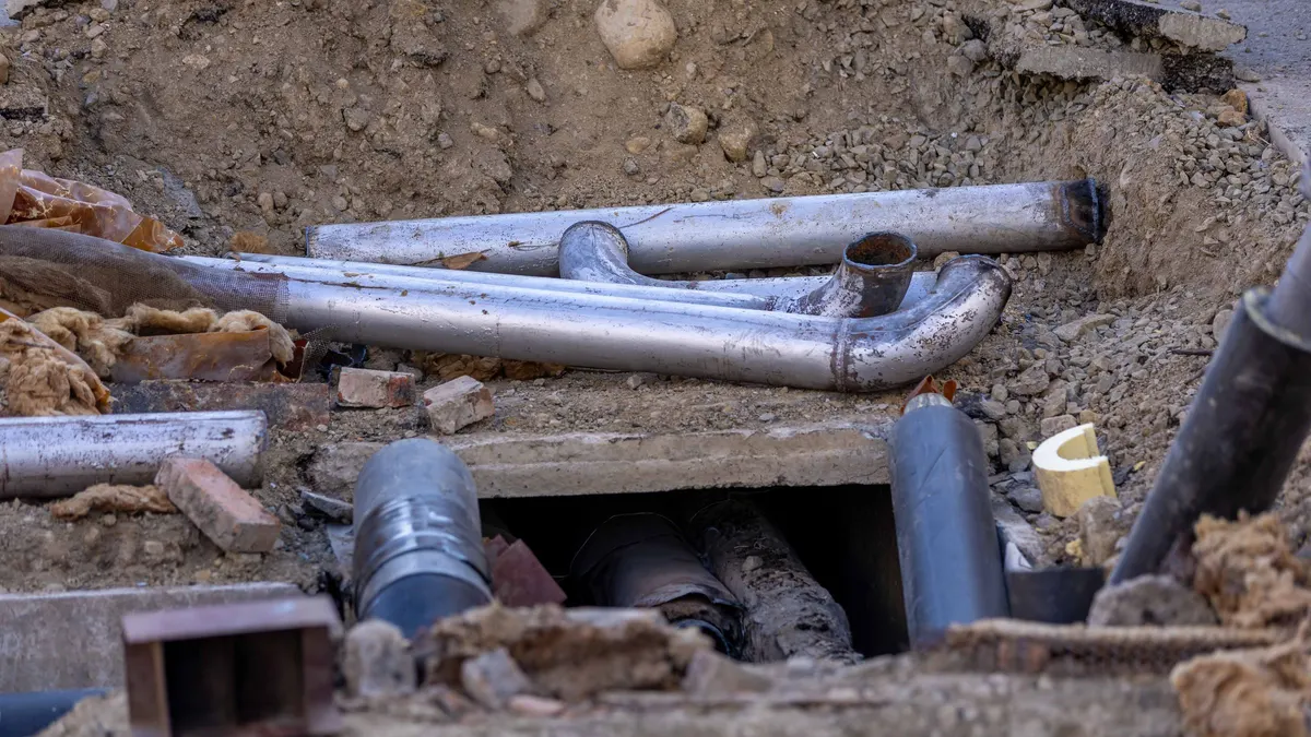 Pipes laid in excavated ground beside a building foundation