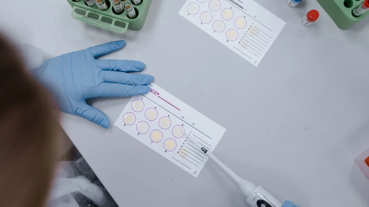 Gloved hands handling a test sample sheet on a laboratory bench