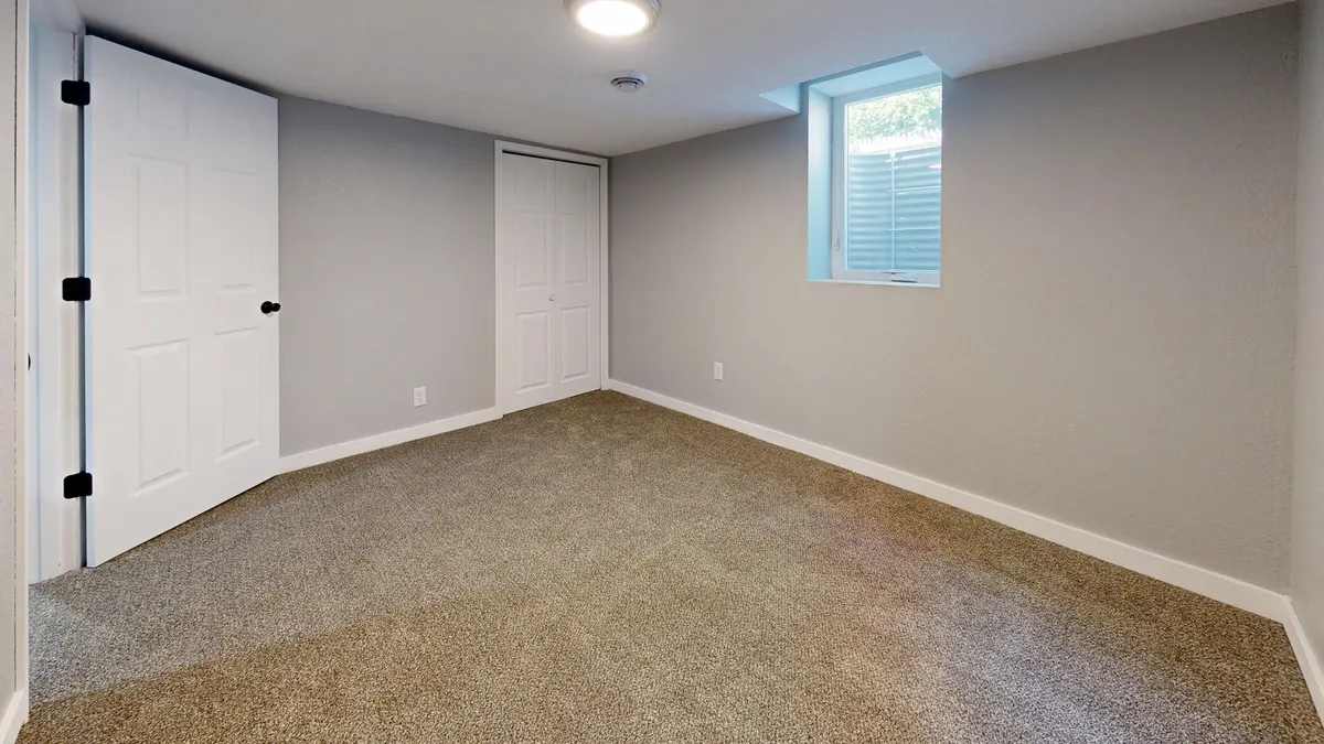An empty finished basement room with a small window and carpeted floor