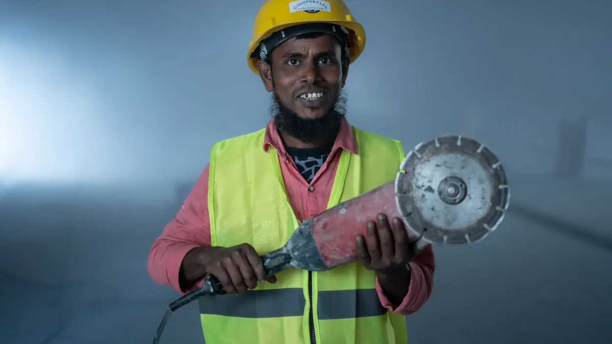 A worker in a hard hat and high-visibility vest holding a diamond cutting blade