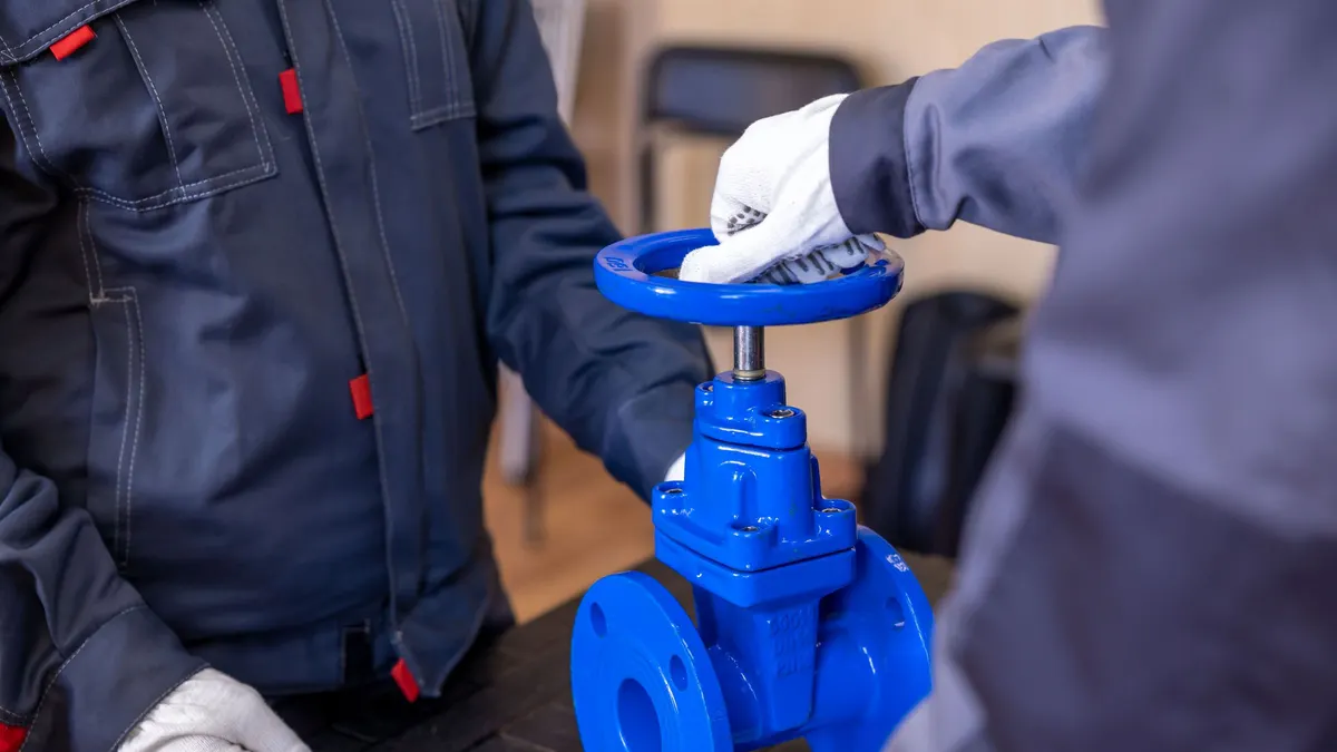 Two technicians in gloves adjusting a blue industrial gate valve