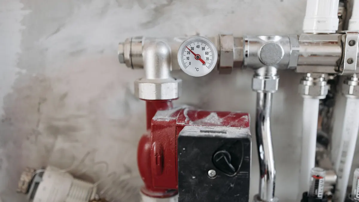 A red circulation pump and pressure gauge mounted on white plumbing pipes