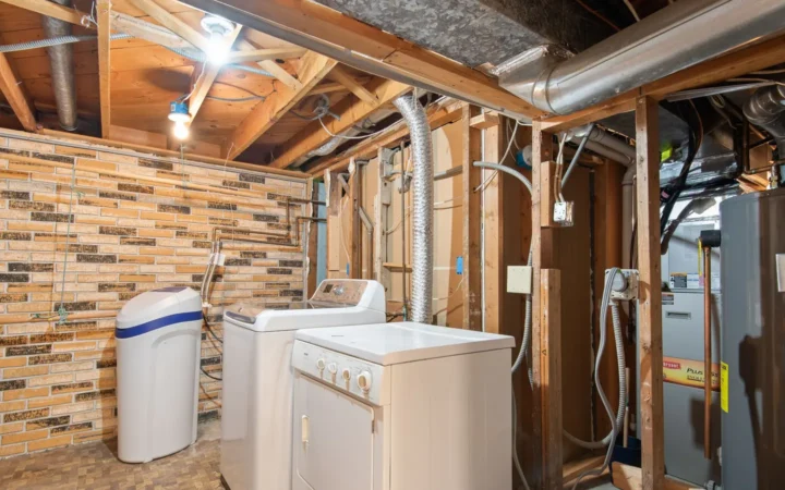 A home utility room with exposed water pipes, a water treatment tank and laundry appliances