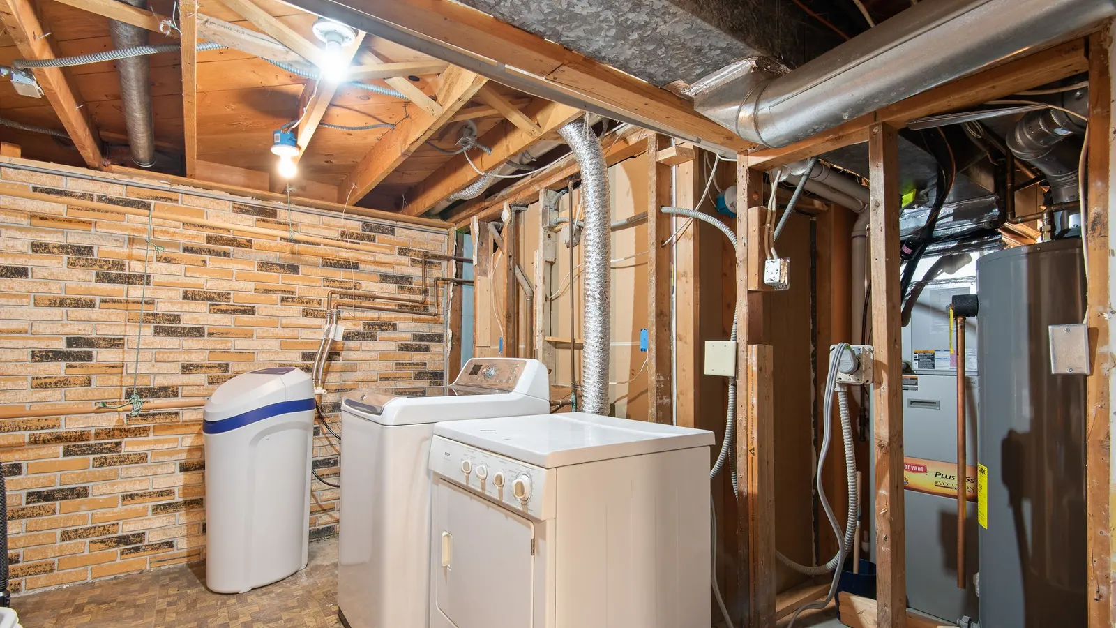 A home utility room with exposed water pipes, a water treatment tank and laundry appliances