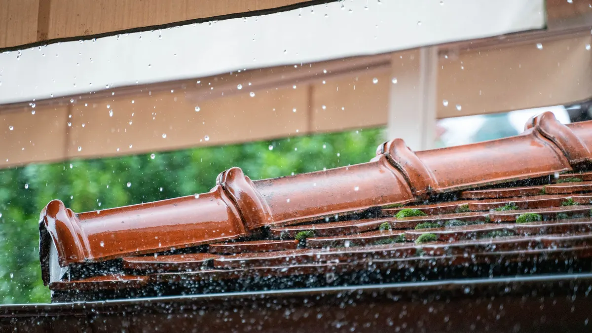 Rain water cascading off the edge of a terracotta tiled roof
