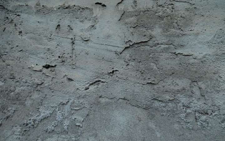 A textured concrete wall with fine cracks and uneven surface staining