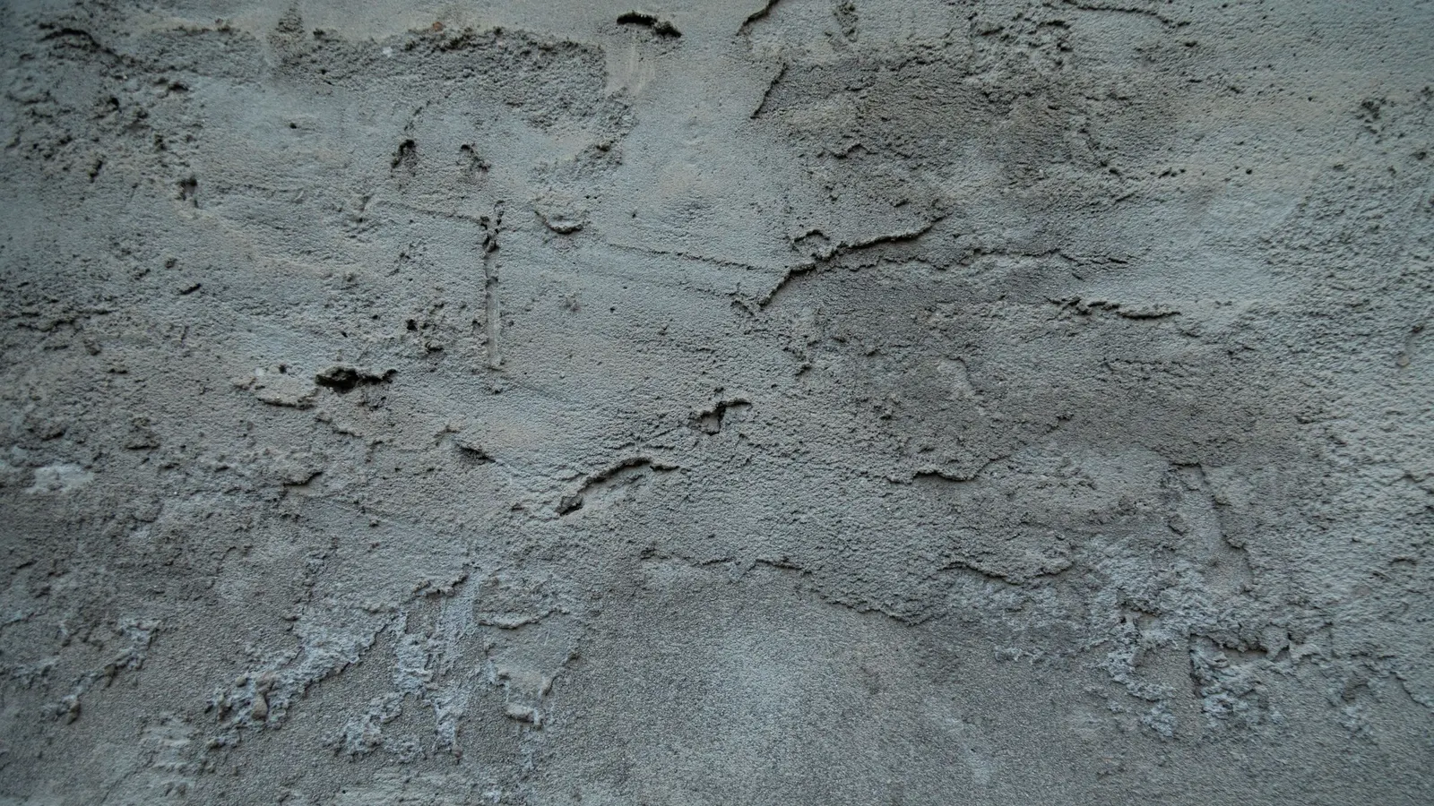 A textured concrete wall with fine cracks and uneven surface staining