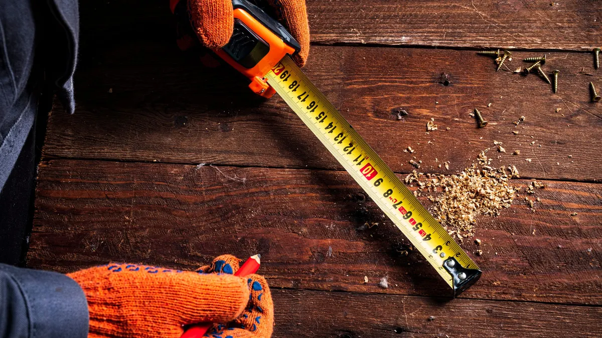 A gloved hand extending a tape measure across a timber surface